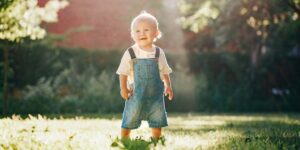 Cute baby boy standing in park outdoor at sunset. Adorable smili